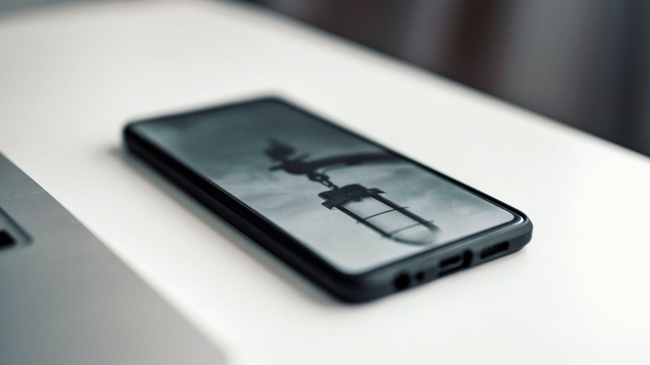 Gros plan sur un smartphone affichant une image floue, posé sur un bureau à côté d’un ordinateur portable.